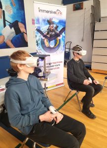 Two youth sitting with Oculus headsets on in front of an ORIGIN pull up banner. 